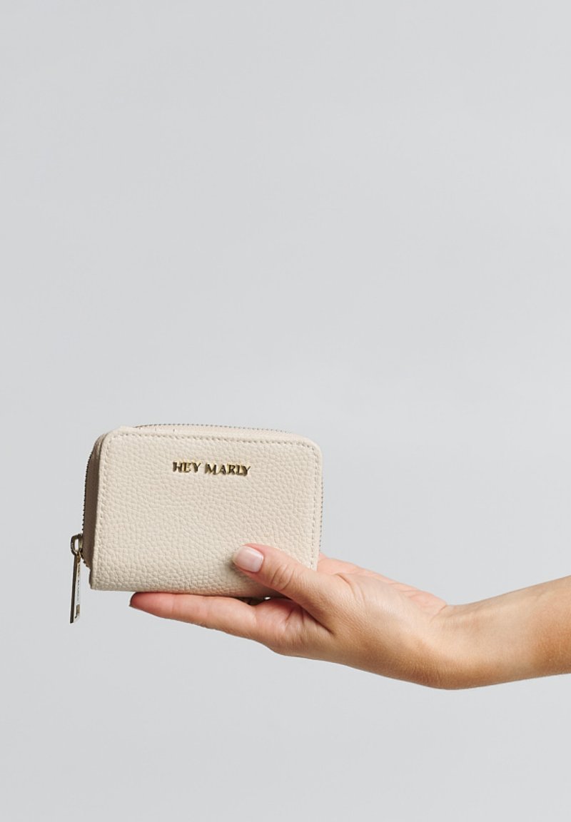 Beige textuur portemonnee met een ritsluiting. Voorzien van 'HEY MARLY' in goud gedrukt op de voorkant, vastgehouden in een hand tegen een lichte achtergrond.