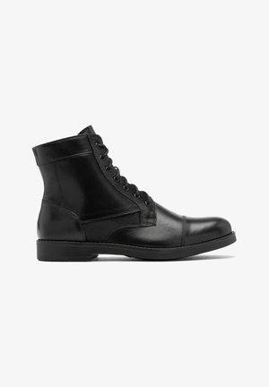 Czarne skórzane botki za kostkę o gładkim wykończeniu, z okrągłym czubkiem i sznurowanym designem. Zawierają detale w postaci szwów oraz solidną gumową podeszwę.