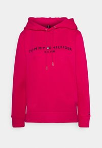 Różowa bluza z kapturem wykonana z bawełny, z długimi rękawami, kapturem z regulowanym sznurkiem oraz czarno wyhaftowanym logo „TOMMY HILFIGER”.