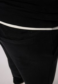 Sorte joggers med en hvid talje, lavet af blødt stof. Har en baglomme og diskret tekstureret logo detalje.