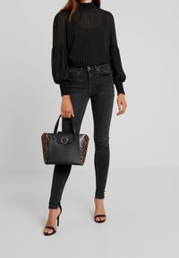 Blusa negra de mangas largas con plisados, combinada con jeans ajustados negros. Lleva un bolso de mano con estampado de serpiente en negro y marrón, con un acento de hardware circular.