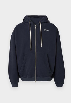 Tmavě modrá mikina na zip z měkké látky má přední kapsu, kapuci se stahovací šňůrkou a vyšívané logo na hrudi. Hladká textura.