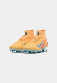 Bottines de football Nike en orange vif avec des accents bleus, tige texturée, design à col haut et semelle à crampons transparente.