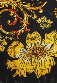Svart tyg med ett blommönster som har stora gula och vita blommor samt oranga inslag, som visar intrikata virvlar och mönster.