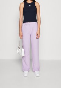 Černý bezrukávový crop top s hvězdným akcentem; levandulové široké kalhoty; bílá kabelka; bílé tenisky; hladké textury po celém outfitu.