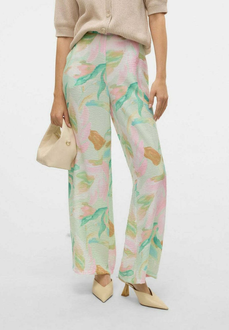 Pantaloni a gamba larga con fantasia floreale in colori pastello (verde, rosa, beige) con una finitura testurizzata, abbinati a una borsa color crema e scarpe con punta.