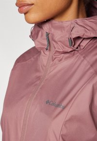 Lightweight, pink Columbia jacket with a high collar, zip closure, and adjustable toggle. Features logo detail and smooth fabric texture.