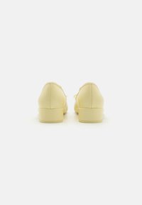 Zapatos de cuero amarillos con textura suave, punta redondeada, pequeño tacón y diseño con cordones, vistos desde la parte de atrás.