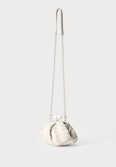 Petit sac à main en tissu beige avec un motif circulaire subtil, une bandoulière chaîne argentée et une fermeture arrondie avec deux perles blanches.
