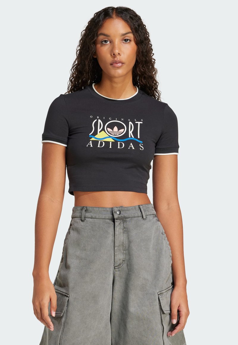 Černé zkrácené tričko s bílým lemem a barevným logem Adidas. V kombinaci s šedými cargo kalhotami s vysokým pasem a bočními kapsami.