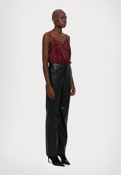Bordeaux satijnen camisole met kantdetails, gecombineerd met hoogmatige zwarte leren broeken en puntige zwarte hakken. Minimalistisch ontwerp.