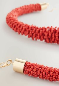 Collar de cuentas rojas compuesto por pequeñas cuentas redondeadas. Los extremos están rematados con acentos de metal dorado. Diseño texturizado con cierre de broche.
