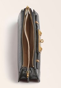 Musta teksturoitu nahkainen käsilaukku, jossa on kultaiset metalliosat, kaksinkertaiset vetoketjut ja sileä sisäpuoli. Ominaisuuksina kulmikkaat yksityiskohdat ja jämäkkä muoto.