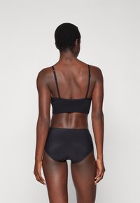 Black bralette with adjustable straps and seamless design paired with high-waisted black underwear, showcasing a smooth texture.