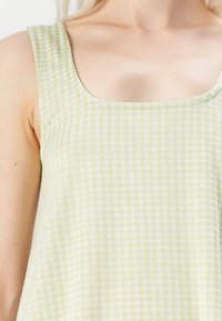 Top em gingham verde claro com decote quadrado e alças largas. O tecido tem uma textura suave e um padrão de grade em verde claro e escuro.