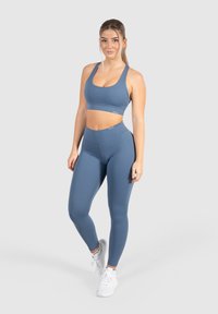 Set di reggiseno sportivo blu e leggings, realizzato in tessuto elasticizzato. Presenta un design con ritagli sui lati, una texture liscia e dettagli di branding discreti.