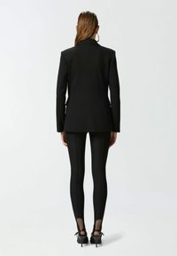 Crni sako sa strukturiranim ramenima, kombiniran s crnim tajicama koje imaju prozirne detalje na gležnjevima i cipelama na visoku petu.