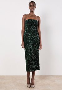 Ohne Träger grünes Pailletten-Midi-Kleid mit einer figurbetonten Silhouette, glatter Textur und subtiler Schimmerung, kombiniert mit hellbeigen High Heels.