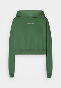 Hoodie verde corto con maniche lunghe e testo bianco "WRSTBHVR STUDIO" centrato sul davanti.
