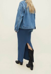 Spijkerjack in lichtblauw, geribbelde lange rok in donkerblauw met een hoge zijsplit, en zwarte heeled laarzen met een ritsdetail.