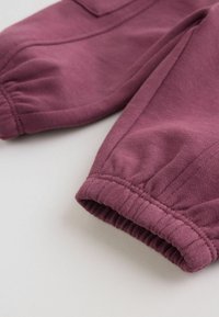 Poignets de manches d'un vêtement mauve avec ourlets élastiqués froncés et coutures visibles sur une surface en tissu doux.