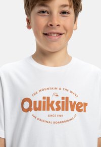 Bílý bavlněný tričko s oranžovým kruhovým logem s nápisem "Quiksilver". Krátké rukávy a design s kulatým výstřihem.