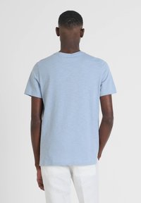 Camiseta de manga corta azul claro, fabricada con tejido suave, con un cuello redondo y un dobladillo recto. La vista trasera muestra una superficie lisa, sin adornos.