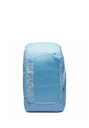 Mochila Reebok azul claro con bolsillo frontal de malla, cierre de cremallera y logo "Reebok" en el lado izquierdo.