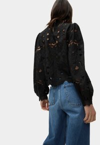 Blusa di pizzo nero con motivi floreali, maniche a sbuffo e orlo a scallop, abbinata a jeans in denim azzurri a vita alta.