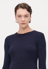 Top a maglia a coste blu navy con maniche lunghe e colletto rotondo. La texture è liscia e la forma aderente mette in risalto il torso.