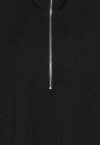 Svart topp med hög krage som har ett silvrigt dragkedjedetalj framtill. Tyget verkar slätt och mjukt i textur.