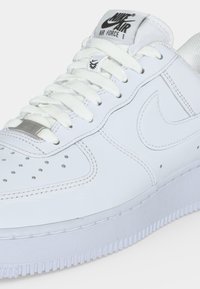 Λευκό sneaker Nike Air Force 1 με λεπτομερείς ραφές, κορδόνια, τρύπες και το λογότυπο Nike στο πλάι και στη γλώσσα.