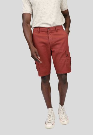 Shorts cargo rouges avec poches latérales, fermeture à bouton et passants de ceinture, associés à un t-shirt texturé gris clair et des baskets montantes blanches.