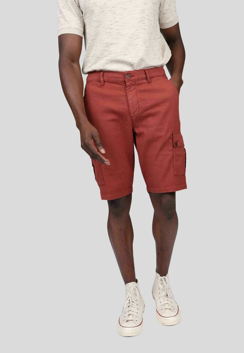 Shorts cargo rouges avec poches latérales, fermeture à bouton et passants de ceinture, associés à un t-shirt texturé gris clair et des baskets montantes blanches.