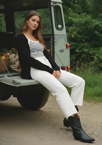 Black cardigan, striped tank top, high-waisted white pants, and black cowboy boots. Sitting on a truck tailgate, green background.