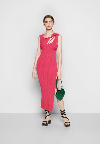 Vestido justo canelado em rosa vivo com detalhes recortados. Combinado com sandálias de plataforma pretas com tiras e uma bolsa em forma de coração verde.