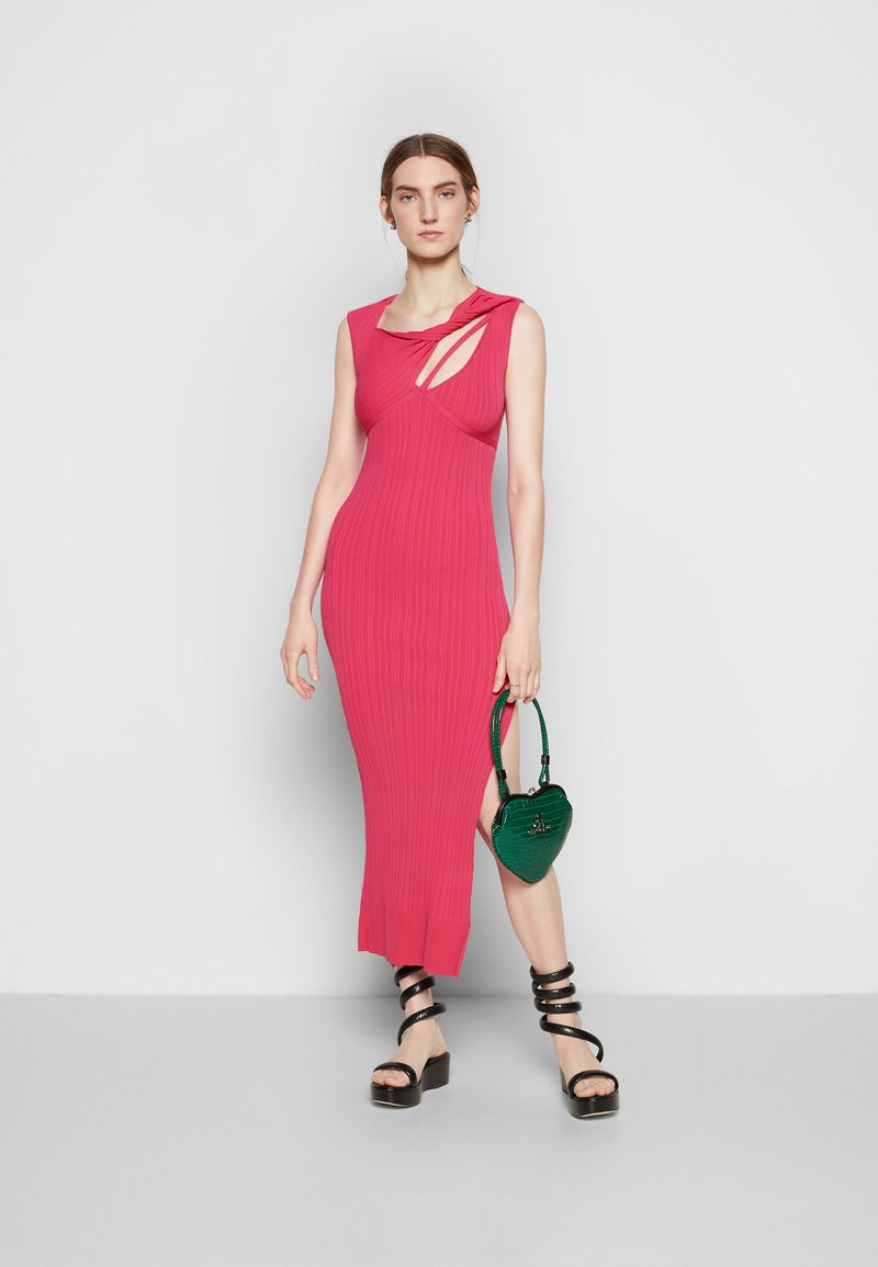 Robe côtelée ajustée en rose vif avec des découpes. Associée à des sandales à plateforme noires avec des lanières et un sac à main en forme de cœur vert.