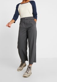 Grå högmidjade byxor med ett bälte, med en tapered ben-design. Matchas med en krämfärgad och marinblå långärmad skjorta och beige vandringskängor.