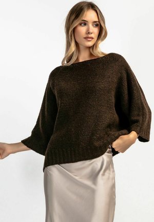 Brązowy, oversize sweter dzianinowy z szerokimi rękawami i ściągaczem na dole, w zestawieniu z jasną satynową spódnicą, eksponującą fakturowany materiał.