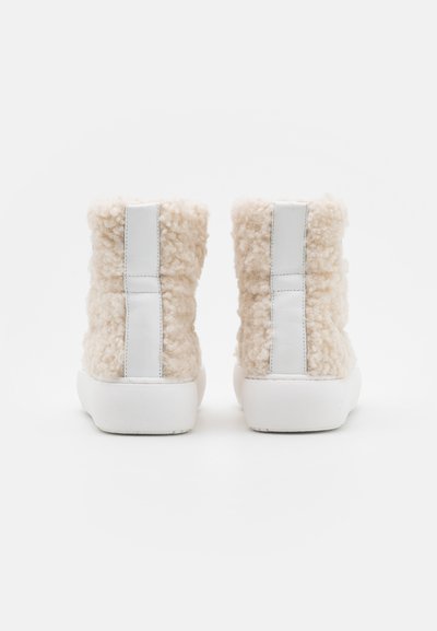 Botas de tornozelo bege fofas com material texturizado suave, detalhes em couro branco e uma sola branca grossa com um acabamento suave.