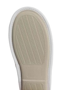 Suela de un zapato con una base de goma texturizada, material lateral blanco y una entresuela suave de color beige con un patrón elevado para mejorar el agarre.