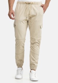 Pantalones jogger cargo beige hechos de tela ligera, con cintura elástica con cordón, bolsillos laterales y puños elásticos en los tobillos.