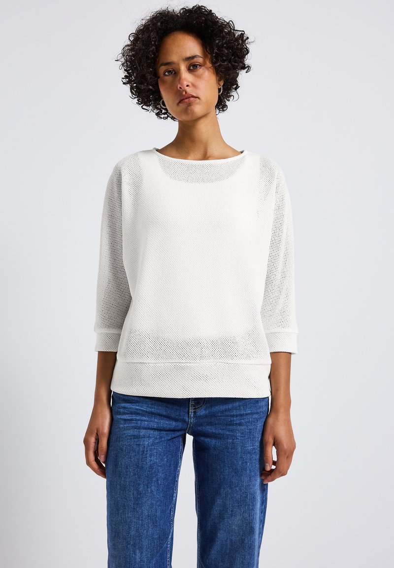 Witte mesh top met lange mouwen en een brede halslijn, met driekwartmouwen, gemaakt van getextureerde stof en een losse pasvorm. Gecombineerd met blauwe denim jeans.