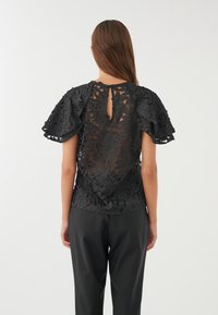 Top nero con un design in pizzo floreale, maniche corte a volants e un'apertura a chiave sul retro con chiusura a bottone. Abbinato a pantaloni.