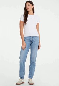 Camiseta blanca ajustada con bordado negro, combinada con jeans de pierna recta de color azul claro. Los zapatos son de color beige y marrón claro con un diseño deportivo.