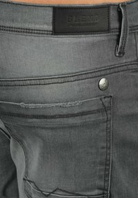 Gray denim jeans with a black leather label, featuring subtle stitching details and a metal button. Back pocket design visible.