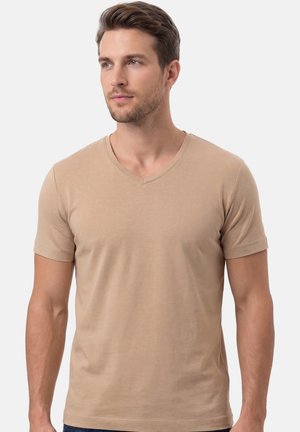Young man with light skin and brown hair wearing a beige V-neck short-sleeve T-shirt, looking slightly left, neutral background.