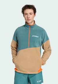 Fleece pullover in teal and tan with orange accents. Features a half-zip collar and front pocket. Logo displayed on chest. Soft texture.