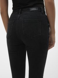 Jeans de mezclilla negra con un corte ajustado, que presentan una cintura de altura media, bolsillos traseros característicos y una tela texturizada. Diseño simple sin adornos.