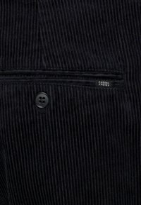 Černá kordová tkanina s knoflíkovou zadní kapsou a malou černou etiketou s nápisem "CASUAL FRIDAY."